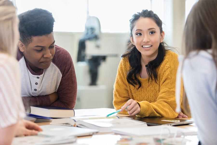 Female High school student pointing to a document at a table sitting with two other students..